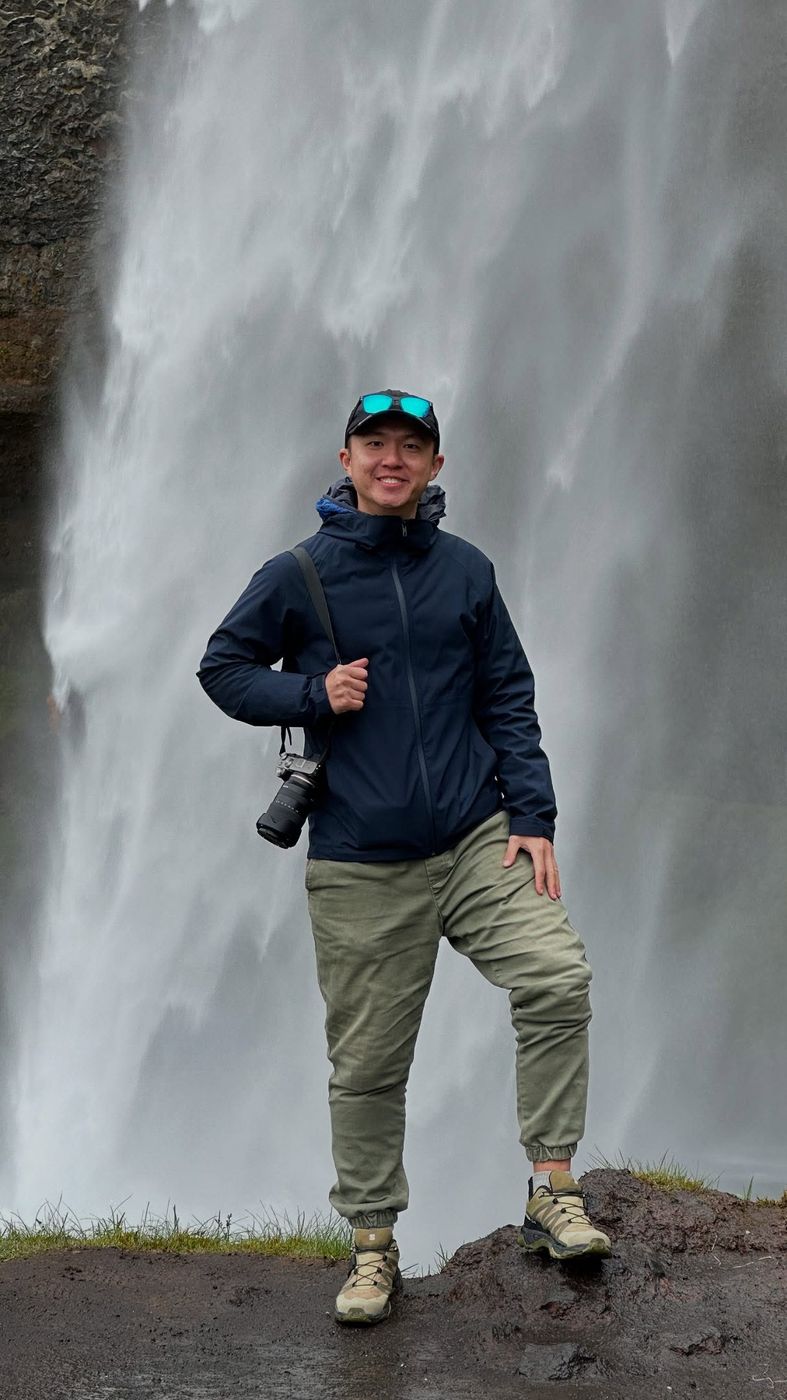 Andrew standing in front of a waterfall in Iceland, camera over his shoulder.